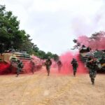 Soldiers running from armored vehicles with red smoke.