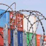 shipping containers stakced behind barbed wire
