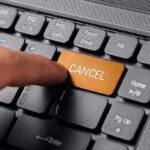 Finger pressing a cancel button on a keyboard.