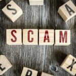 Wooden blocks spell "SCAM" on a rustic surface.