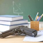 Nation Mourns After School Shooting Claims Multiple Lives Gun on desk with school supplies and books.