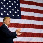Trump Jr. Visits Greenland Amid Father’s Push to Make It Part of America Man clapping in front of large American flag