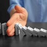 Hand stopping falling row of dominoes.