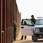 DHS Secretary Announces New Construction On Border Wall Border patrol agents near a tall metal fence.
