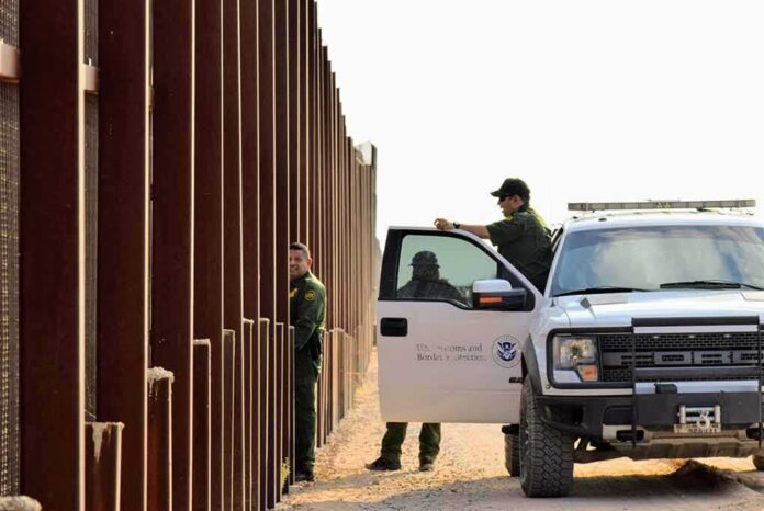 1545833798 featured image Border patrol agents near a tall metal fence.