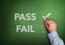 Hand checking "Pass" box on chalkboard.