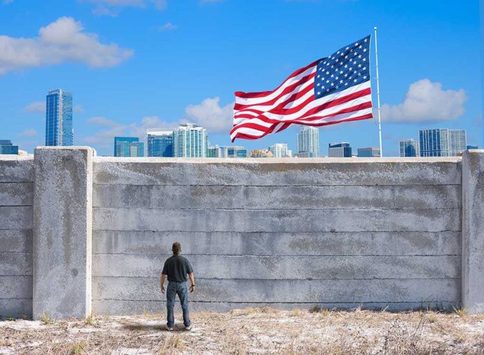 571768102 featured image Man standing by tall concrete wall with American flag