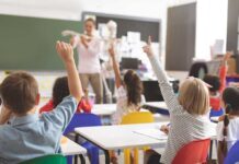 Children raising hands in classroom.