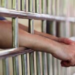 Hands clasped behind metal prison bars