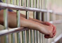 Hands clasped behind metal prison bars