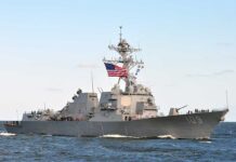 Military ship sails with American flag.
