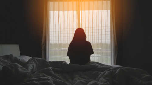 shutterstock_1439614217.jpg featured image Silhouette of person sitting on bed facing window.
