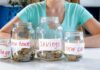 Four labeled jars filled with coins on table