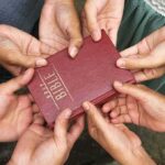 Multiple hands holding a red Bible together