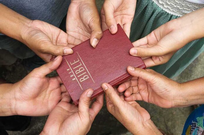 133452947 featured image Multiple hands holding a red Bible together
