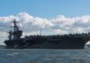 Aircraft carrier on water under a cloudy sky.