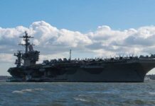 Aircraft carrier on water under a cloudy sky.