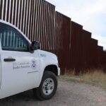 Border protection vehicle near a large metal fence.
