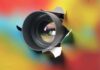 Camera lens poking through torn colorful background