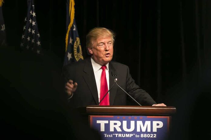 403318090 featured image Man speaking at podium with TRUMP sign.
