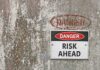 Danger Risk Ahead sign on weathered wall.