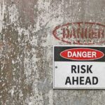 Danger Risk Ahead sign on weathered wall.