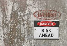 Danger Risk Ahead sign on weathered wall.