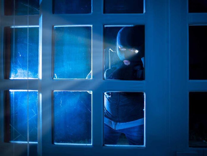 514808032 featured image Masked figure peering through glass door at night.