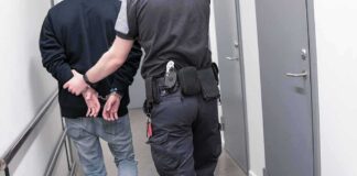 Officer escorting handcuffed person down hallway