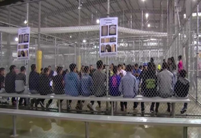 People sitting on benches inside a fenced facility