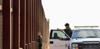 Border patrol agents near a tall metal fence