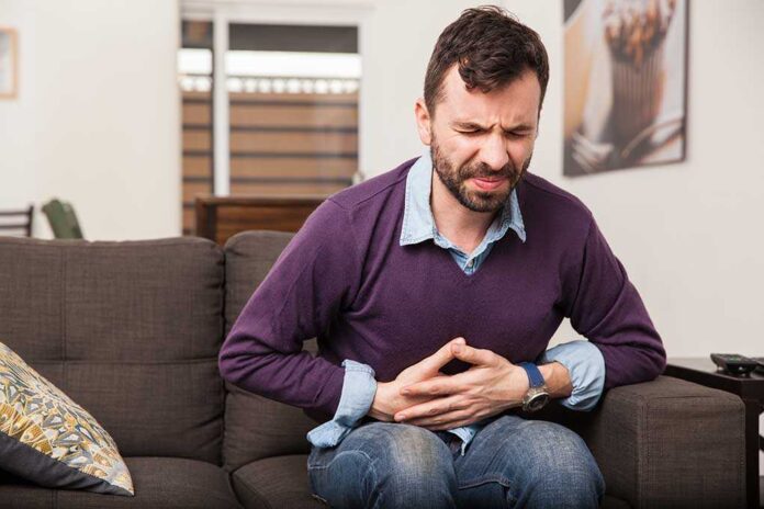 344063903 featured image Man sitting on couch holding stomach in pain
