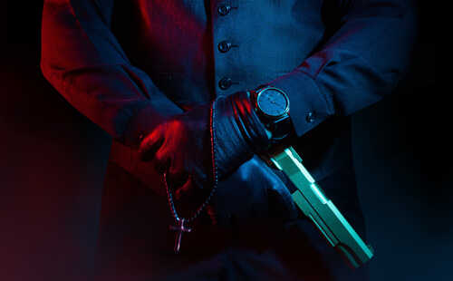 shutterstock_1831527514.jpg featured image Man holding gun and rosary with cross.