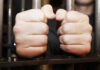 Hands gripping jail cell bars tightly