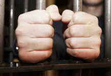 Hands gripping jail cell bars tightly