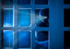 Masked figure peering through glass door at night