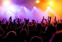 Crowd at a concert with raised hands and colorful stage lights