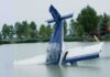 A submerged airplane partially in a lake with trees in the background