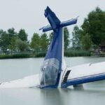 A submerged airplane partially in a lake with trees in the background