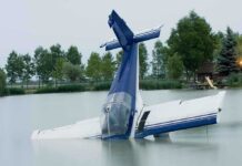 A submerged airplane partially in a lake with trees in the background