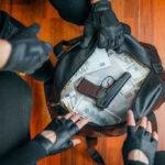 Gloved hands around bag with money and gun.