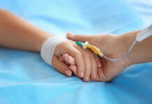 Two hands holding, one with medical IV attached