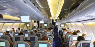 Interior view of an airplane with passengers seated and using inflight entertainment screens