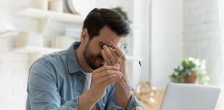 Man rubbing eyes holding glasses near laptop