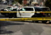 Police tape blocking street with patrol cars.