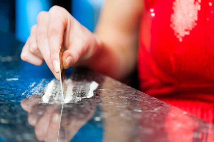 A hand using a card to prepare a line of white powder on a reflective surface