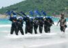 Group of military personnel in wetsuits carrying paddles while wading through the ocean