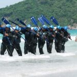 Scientists Race Against Shark KILLING Spree Group of military personnel in wetsuits carrying paddles while wading through the ocean