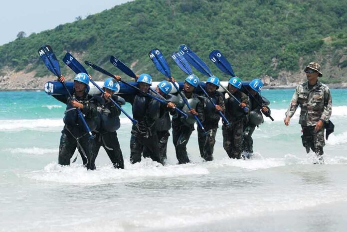 Group of military personnel in wetsuits carrying paddles while wading through the ocean