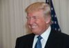 A smiling man in formal attire with an American flag in the background